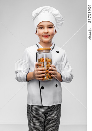 smiling boy in chef's toque holding jar with pasta 87733936