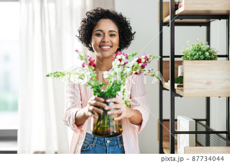 smiling woman holding flowers in vase at home smiling woman holding flowers in vase at home 87734044