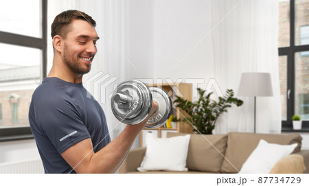 smiling man exercising with dumbbell at home 87734729