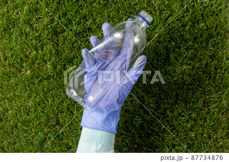 hand in glove picking plastic bottle from grass hand in glove picking plastic bottle from grass 87734876