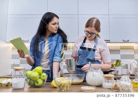 Mother and teenage daughter cooking at home in the kitchen. Mother and teenage daughter cooking at home in the kitchen. 87735396