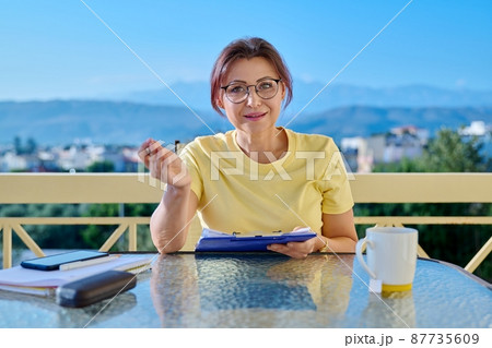 Portrait of business woman looking at webcam while sitting at home office desk Portrait of business woman looking at webcam while sitting at home office desk 87735609