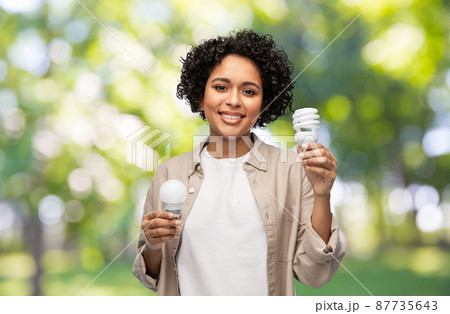 smiling woman holding lighting bulbs over green smiling woman holding lighting bulbs over green 87735643