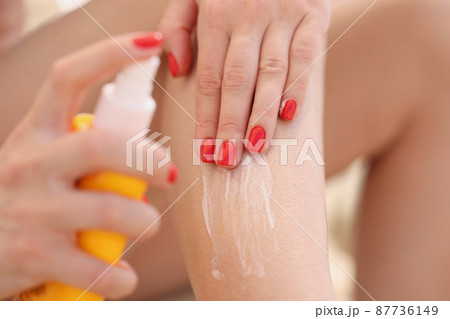 Female applying sunscreen lotion on legs, female with red manicure, protect body from sun Female applying sunscreen lotion on legs, female with red manicure, protect body from sun 87736149