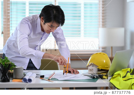 Asian male construction engineer working with blueprint in office. 87737776