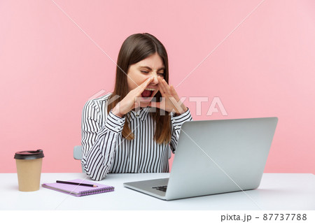 Nervous angry business woman in striped shirt loudly screaming holding hands near mouth, talking video conference sitting at workplace. Indoor studio shot isolated on pink background Nervous angry business woman in striped shirt loudly screaming holding hands near mouth, talking video conference sitting at workplace. Indoor studio shot isolated on pink background 87737788