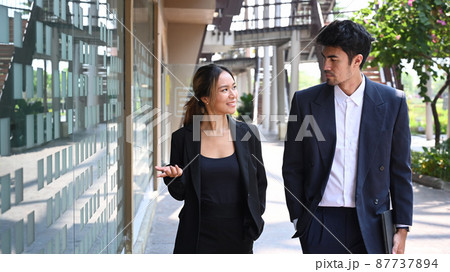 Two young business colleagues discussing business while walking outside office. Two young business colleagues discussing business while walking outside office. 87737894