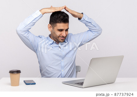 Safety insurance, secured life. Positive man agent sitting office workplace, talking with client on video call and showing house roof gesture over head. indoor studio shot isolated on white background Safety insurance, secured life. Positive man agent sitting office workplace, talking with client on video call and showing house roof gesture over head. indoor studio shot isolated on white background 87737924