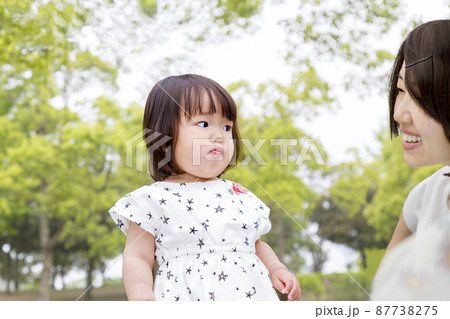 新緑の樹木を背景に母と一緒に遊び飽きた顔をする幼い女の子。育児,教育,教育,躾のイメージ 87738275