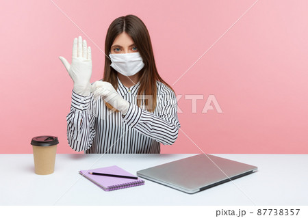 Protection against coronavirus infection. Woman office employee sitting at workplace, feeling safe healthy with hygienic face mask and protective gloves during covid-19 quarantine. indoor studio shot 87738357