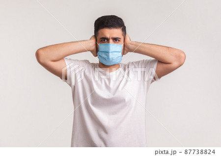 Protection against coronavirus, contagious disease. Man covering ears and wearing hygienic safety mask to prevent infection, respiratory illness such as flu, 2019-nCoV, ebola. studio shot, isolated Protection against coronavirus, contagious disease. Man covering ears and wearing hygienic safety mask to prevent infection, respiratory illness such as flu, 2019-nCoV, ebola. studio shot, isolated 87738824