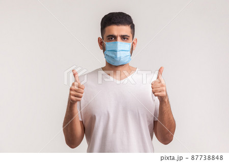 Effective protection against contagious disease. Man showing thumbs up and wearing hygienic mask to prevent infection, respiratory illness such as flu, coronavirus. indoor studio shot, isolated Effective protection against contagious disease. Man showing thumbs up and wearing hygienic mask to prevent infection, respiratory illness such as flu, coronavirus. indoor studio shot, isolated 87738848