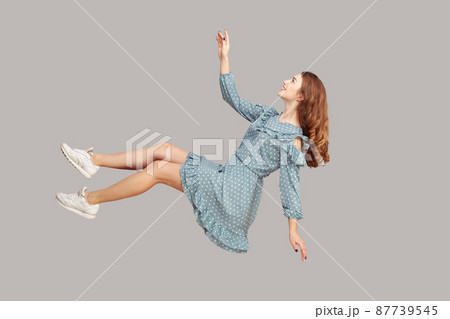 Hovering in air. Cheerful smiling pretty girl in vintage ruffle dress levitating flying in mid-air, looking up happy dreamy and raising hand to catch. indoor studio shot isolated on gray background Hovering in air. Cheerful smiling pretty girl in vintage ruffle dress levitating flying in mid-air, looking up happy dreamy and raising hand to catch. indoor studio shot isolated on gray background 87739545