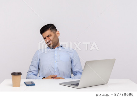 Sudden stomach ache at work. Unhealthy man employee sitting in office, suffering heartburn, gastrointestinal disorder, symptoms of constipation indigestion. studio shot isolated on white background 87739696