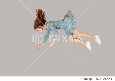 Hovering in air. Relaxed beautiful girl ruffle dress and curly soaring hair levitating, flying in dream with hands up, reaching for something high. indoor studio shot isolated on gray background Hovering in air. Relaxed beautiful girl ruffle dress and curly soaring hair levitating, flying in dream with hands up, reaching for something high. indoor studio shot isolated on gray background 87739723
