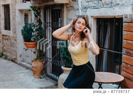 Girl Tourist Walking Through Ancient Narrow Street On A Beautiful Summer Day In MEDITERRANEAN MEDIEVAL CITY, OLD TOWN BUDVA, MONTENEGRO. Young Beautiful Cheerful Woman Walking On Old Street At Girl Tourist Walking Through Ancient Narrow Street On A Beautiful Summer Day In MEDITERRANEAN MEDIEVAL CITY, OLD TOWN BUDVA, MONTENEGRO. Young Beautiful Cheerful Woman Walking On Old Street At 87739737