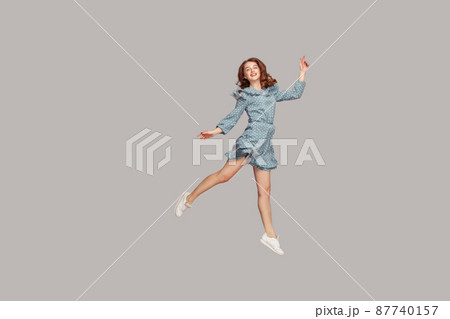 Happy delicate girl in vintage ruffle dress levitating with ballet dance move, hovering in mid-air and smiling joyfully, jumping trampoline, flying up. indoor studio shot isolated on gray background 87740157