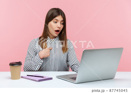 Excited surprised woman office worker pointing herself and looking at laptop screen with amazed expression, talking on video call, online communication. Indoor studio shot isolated on pink background Excited surprised woman office worker pointing herself and looking at laptop screen with amazed expression, talking on video call, online communication. Indoor studio shot isolated on pink background 87745045