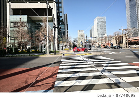 東京交差点風景　車の通行と横断歩道　遠くに八重洲の高層ビル群　青空を衝く高層ビル　横断歩道上の赤い車 87748698