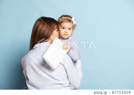 Studio shot of beautiful happy woman and little kid, mother and daughter isolated on blue background. Mother's Day celebration. Concept of family, childhood Studio shot of beautiful happy woman and little kid, mother and daughter isolated on blue background. Mother's Day celebration. Concept of family, childhood 87752029