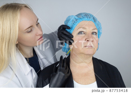 Botulinum toxin injection. Senior woman at the appointment with a beautician who is preparing to give anti-wrinkle injections. Loose skin and hypotension. Mimic wrinkles and contouring Botulinum toxin injection. Senior woman at the appointment with a beautician who is preparing to give anti-wrinkle injections. Loose skin and hypotension. Mimic wrinkles and contouring 87753418