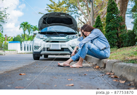 Asian woman sitting beside car after a car breakdown on street. Concept of vehicle engine problem or accident and emergency help from Professional mechanic Asian woman sitting beside car after a car breakdown on street. Concept of vehicle engine problem or accident and emergency help from Professional mechanic 87753870