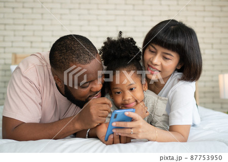 The family has fun and plays education games online with a smartphone at home in the bedroom. Concept of online education and caring from parents. The family has fun and plays education games online with a smartphone at home in the bedroom. Concept of online education and caring from parents. 87753950