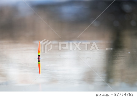 Orange-yellow fishing float in the river water. Spring fishing, bright colors of water and nature. Solar reflection in the water. Background image. 87754765