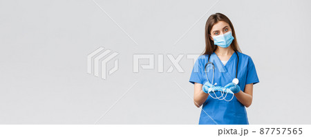 Covid-19, preventing virus, health, healthcare workers and quarantine concept. Attractive female nurse in blue scrubs and personal protective equipment, giving medical masks to patient 87757565