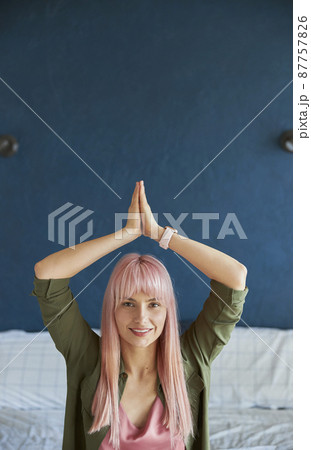 Long haired woman holds hands in namaste mudra above head in bedroom Long haired woman holds hands in namaste mudra above head in bedroom 87757826