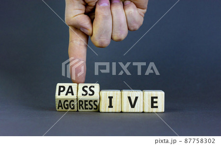 Passive or aggressive symbol. Businessman turns wooden cubes and changes the word passive to aggressive. Beautiful grey background, copy space. Business, psychological passive aggressive concept. 87758302