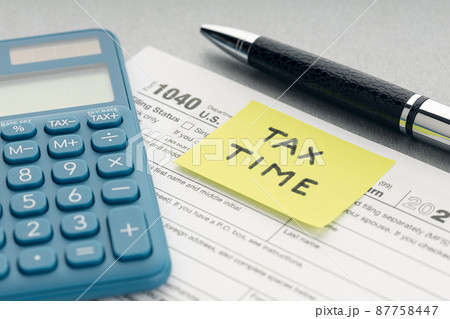 Tax time concept. Yellow note with message, tax form, calculator and pen on table Tax time concept. Yellow note with message, tax form, calculator and pen on table 87758447