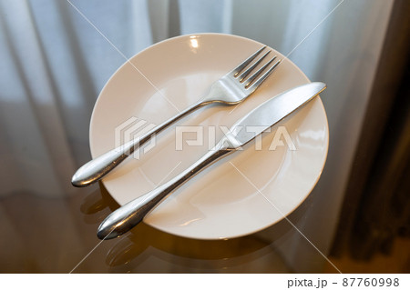 Fork with knife in white plate on glass table 87760998