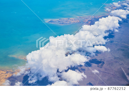 Airplane view of large white clouds over land against ocean coast Airplane view of large white clouds over land against ocean coast 87762252