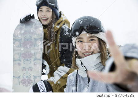 雪の降るスキー場でポーズをするスノボ女子 女子旅の写真素材