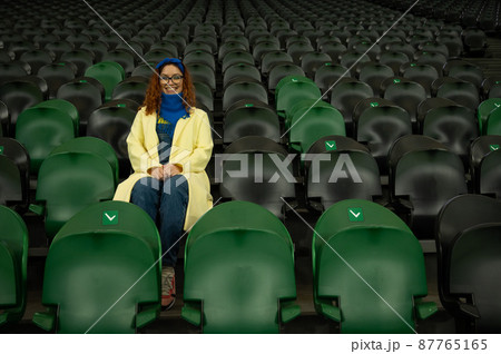 Caucasian woman cheers for a sports team at the stadium. The girl watches the match at the stadium alone. 87765165