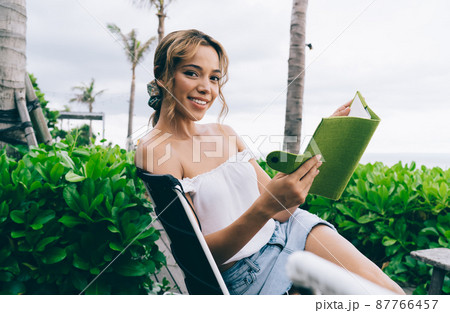 Happy ethnic woman sitting on lounger with notepad 87766457