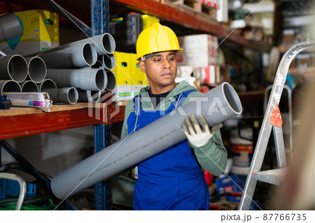Plumber in protective helmet and overalls selects plastic pipes in hardware store 87766735