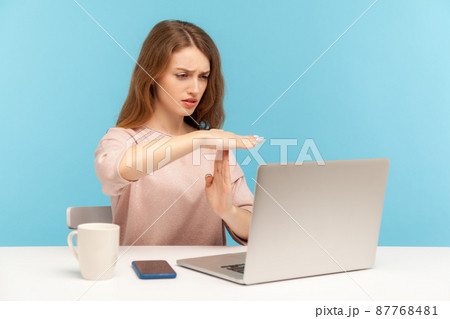 Tired upset woman employee showing time out gesture and looking at laptop screen, talking on video call, asking pause, break of online communication. indoor studio shot isolated on blue background 87768481