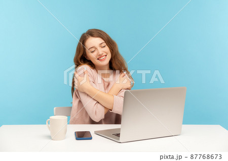 I love myself. Adorable happy woman employee at workplace embracing herself with pleasure expression, feeling proud and satisfied, positive self-esteem. indoor studio shot isolated on blue background I love myself. Adorable happy woman employee at workplace embracing herself with pleasure expression, feeling proud and satisfied, positive self-esteem. indoor studio shot isolated on blue background 87768673