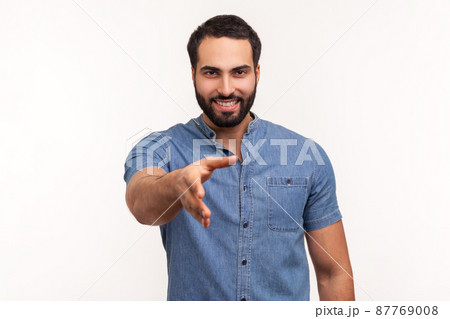 Smiling friendly man with beard in blue shirt holding hand for handshake, happy to make agreement, successful partnership. Indoor studio shot isolated on white background Smiling friendly man with beard in blue shirt holding hand for handshake, happy to make agreement, successful partnership. Indoor studio shot isolated on white background 87769008