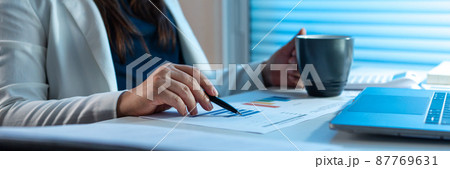 Overwork Concept The office woman who works at her desk pointing her pen on the paper with right hand and holding a cup with her left hand 87769631