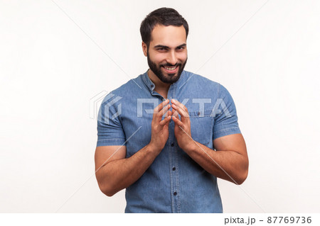 Cunful sneaky man in blue shirt gesticulating with fingers planning devious tricks and cheats, scheming prank, having fun. Indoor studio shot isolated on white background 87769736