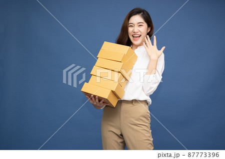 Happy Asian woman smiling and holding package parcel box isolated on deep blue background, Delivery courier and shipping service concept Happy Asian woman smiling and holding package parcel box isolated on deep blue background, Delivery courier and shipping service concept 87773396