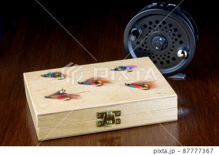 Wooden Fishing Fly Box with Flies and Fly Reel on a Polished Table Top Wooden Fishing Fly Box with Flies and Fly Reel on a Polished Table Top 87777367