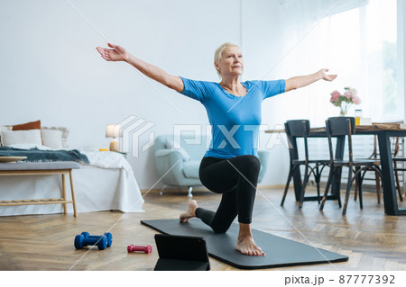 elderly woman doing exercises with an online trainer in her living room. elderly woman doing exercises with an online trainer in her living room. 87777392