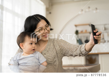 Smiling Asian Young mother and her little son using smartphone at home, taking selfie, Video call. Smiling Asian Young mother and her little son using smartphone at home, taking selfie, Video call. 87778536