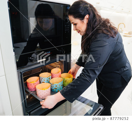 a woman cook puts in the oven dough in paper molds for baking Easter cakes.  87779252
