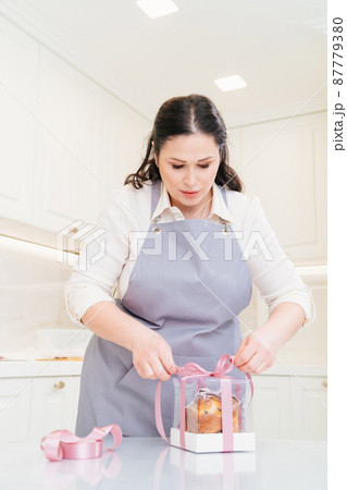 a female cook packs a Kraffin, easter cake in a box with satin ribbon a female cook packs a Kraffin, easter cake in a box with satin ribbon 87779380