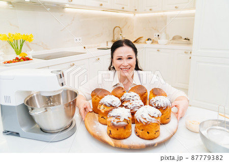 female cook with Kraffins, easter cakes and Panettones in the kitchen. female cook with Kraffins, easter cakes and Panettones in the kitchen. 87779382